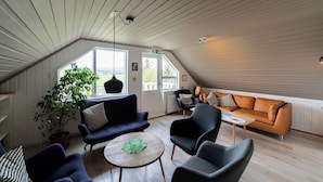 A modern interior with a sloped ceiling, a large window, and a mix of seating options including sofas and chairs. - Hotel Eyvindará (Egilsstaðir)