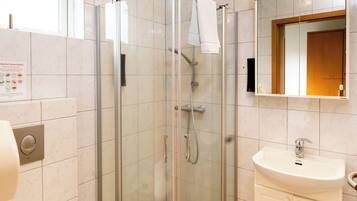 Un baño moderno con ducha de vidrio, lavamanos blanco y espejo sobre él.