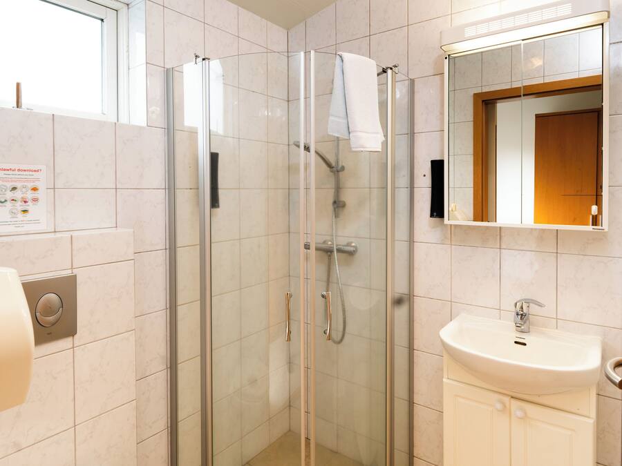 Un baño moderno con ducha de vidrio, lavamanos blanco y espejo sobre él.