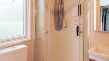 Cabina de ducha con mampara de vidrio, cabezal de ducha de mano, inodoro y lavamanos con espejo superior.
