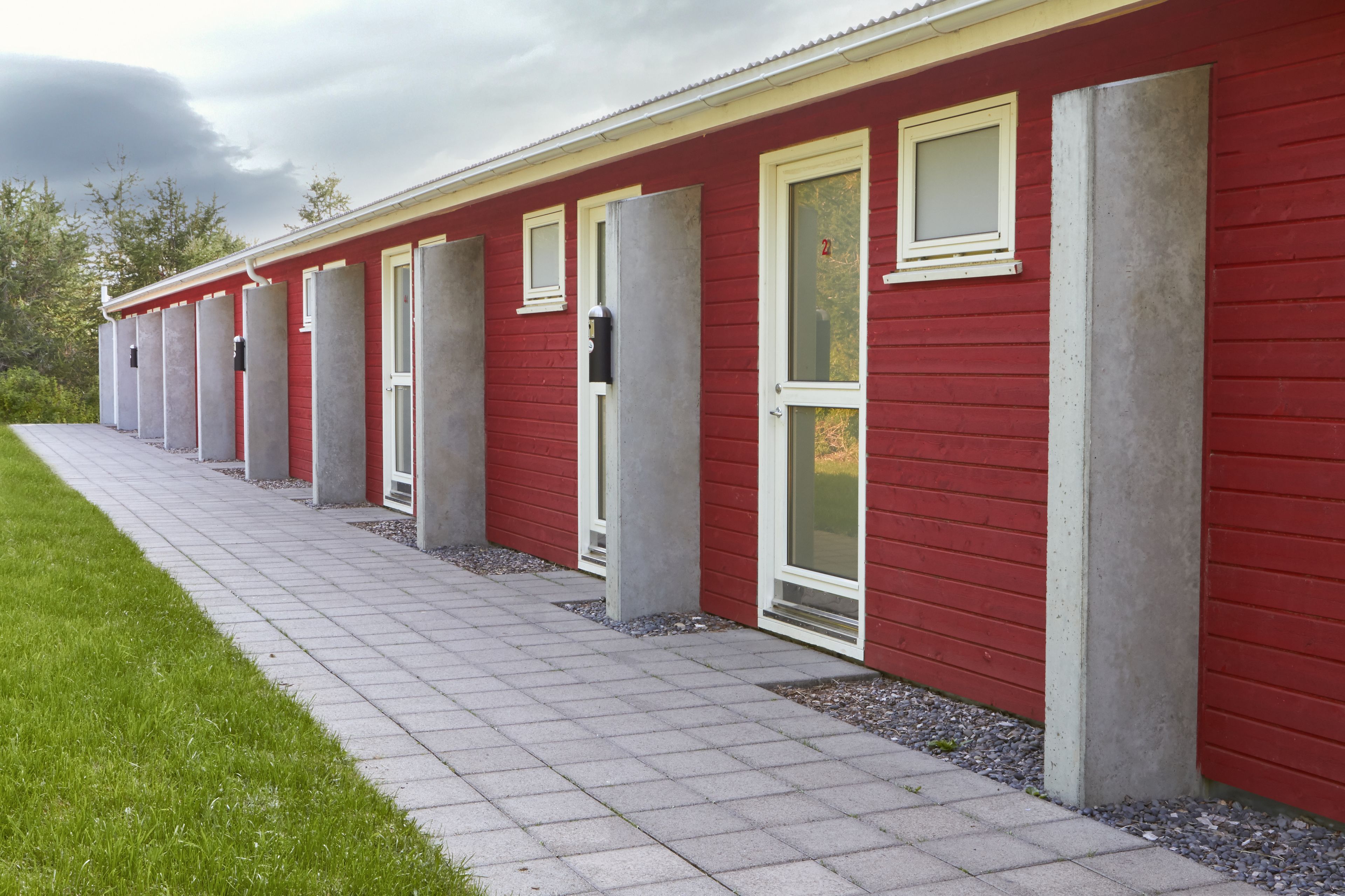 Una hilera de edificios rojos con marcos blancos en ventanas y puertas, un camino pavimentado y un área con césped.