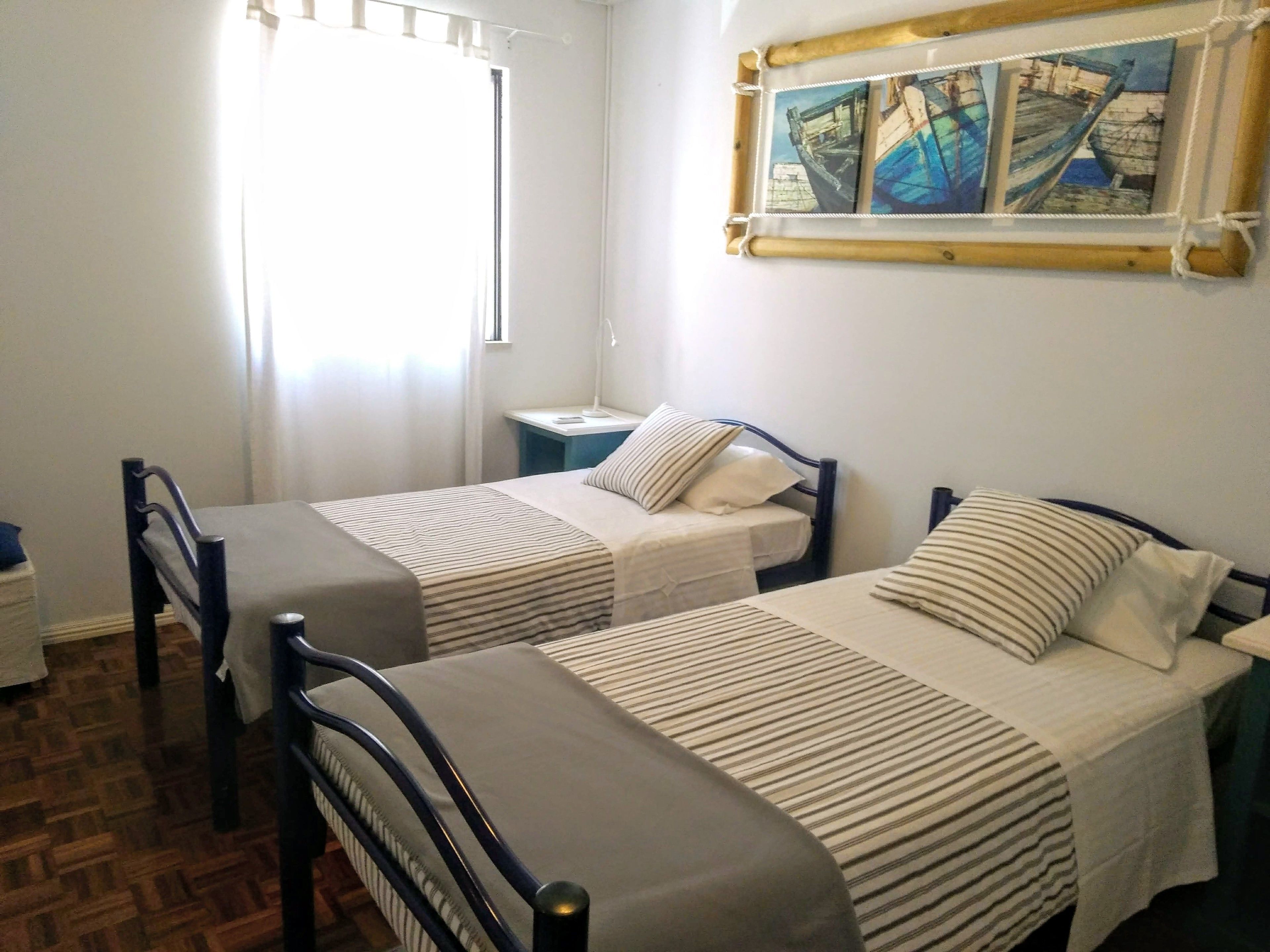 A room with two single beds, a nightstand, a lamp, and a painting on the wall.