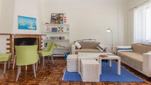 Uma sala de estar com lareira, poltronas verdes, um sofá, uma mesa de centro e uma estante de livros.