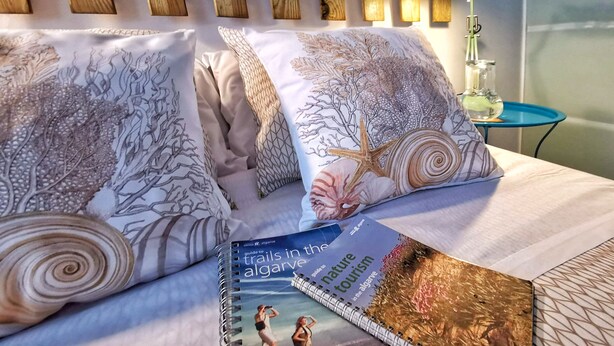 Cama bem arrumada com almofadas estampadas e um guia de viagens em cima.