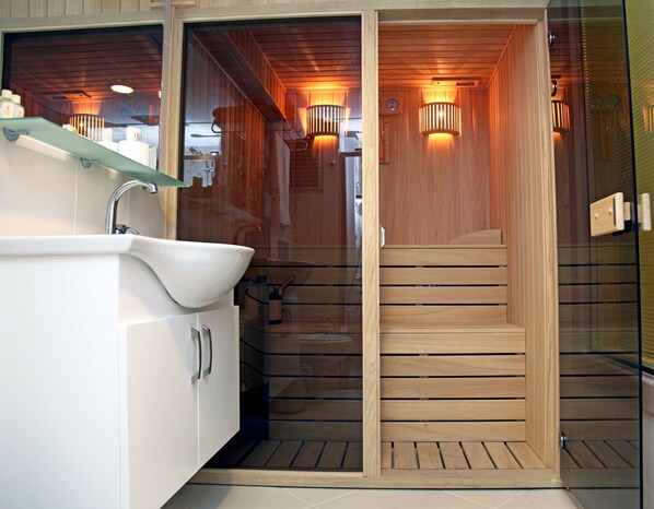Un baño moderno con ducha acristalada, suelo de madera y un lavabo blanco.