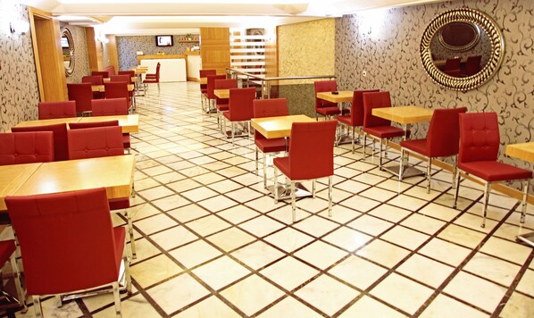 Un restaurante espacioso con cabinas tapizadas en rojo y mesas de madera, suelo de baldosas y un televisor montado en la pared.