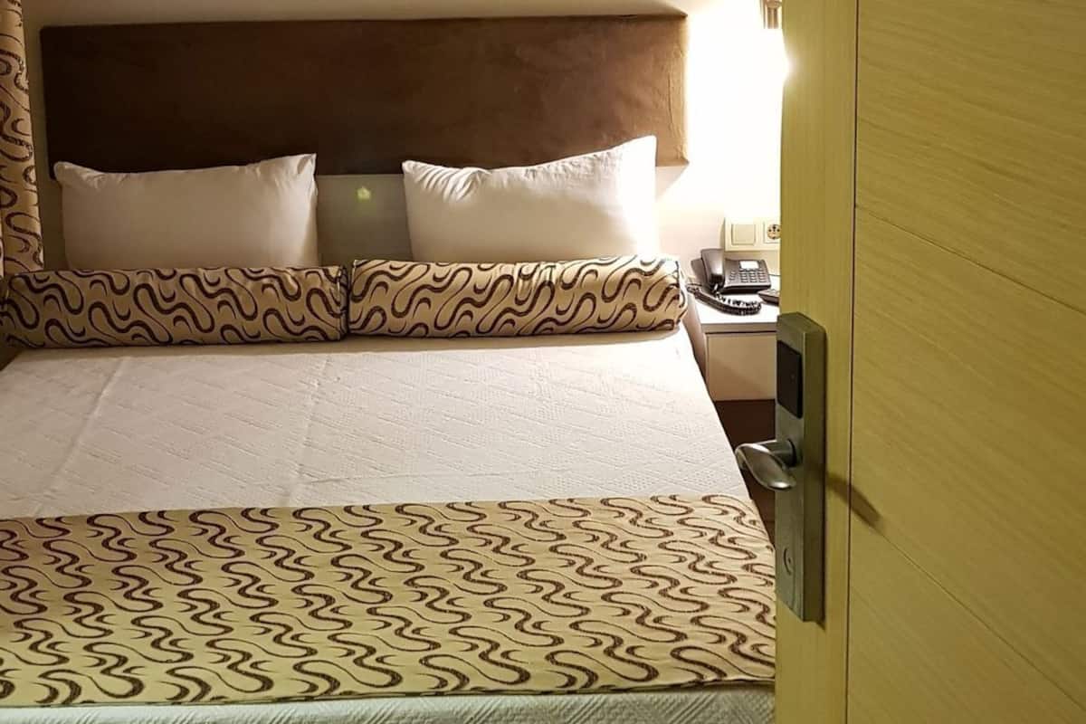 Une chambre d’hôtel équipée d’un lit, d’un appareil de climatisation, d’un téléphone sur la table de chevet et d’une porte portant le numéro de la chambre.
