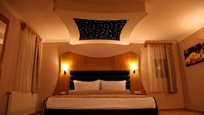 A hotel room with a starry sky ceiling, a large bed with patterned bedding, wooden paneling on the walls, and two wall-mounted lights. - Grand Zeybek Hotel (Izmir)