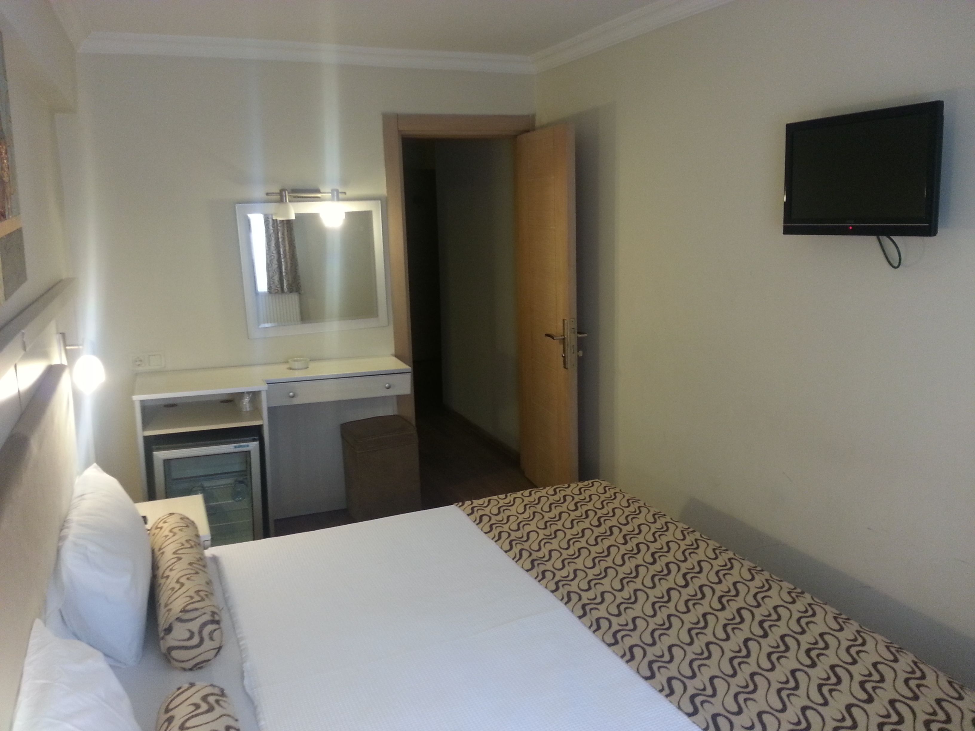 A hotel room with a bed, a desk, a mirror, and a television.