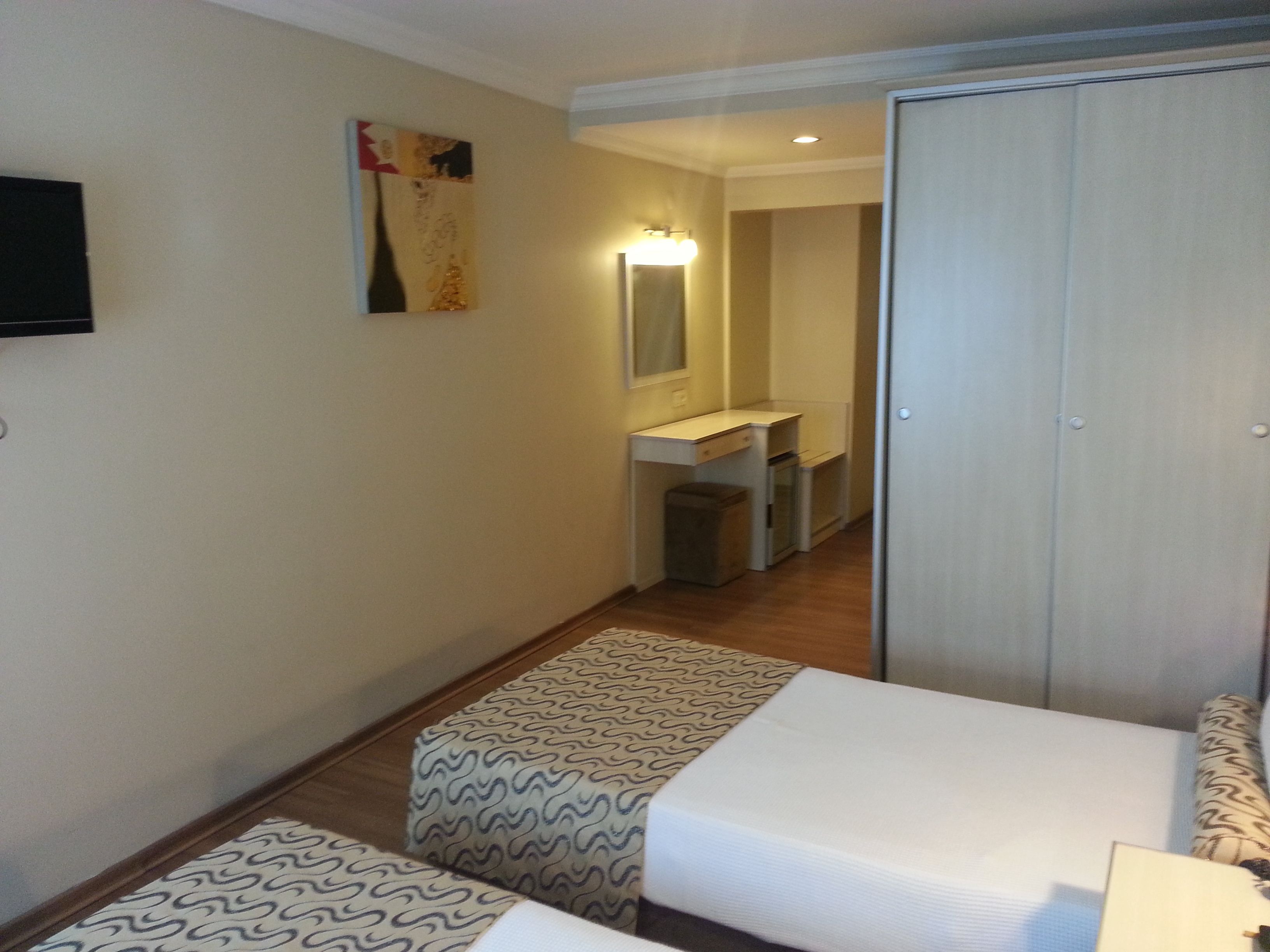 Una habitación de hotel con una cama, una mesita de noche, un espejo, un escritorio pequeño y un armario.