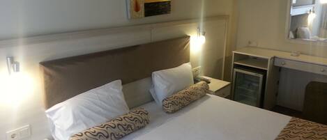 Een hotelkamer met een bed, twee kussens, een nachtkastje, een bureau, een spiegel en een schilderij aan de muur.