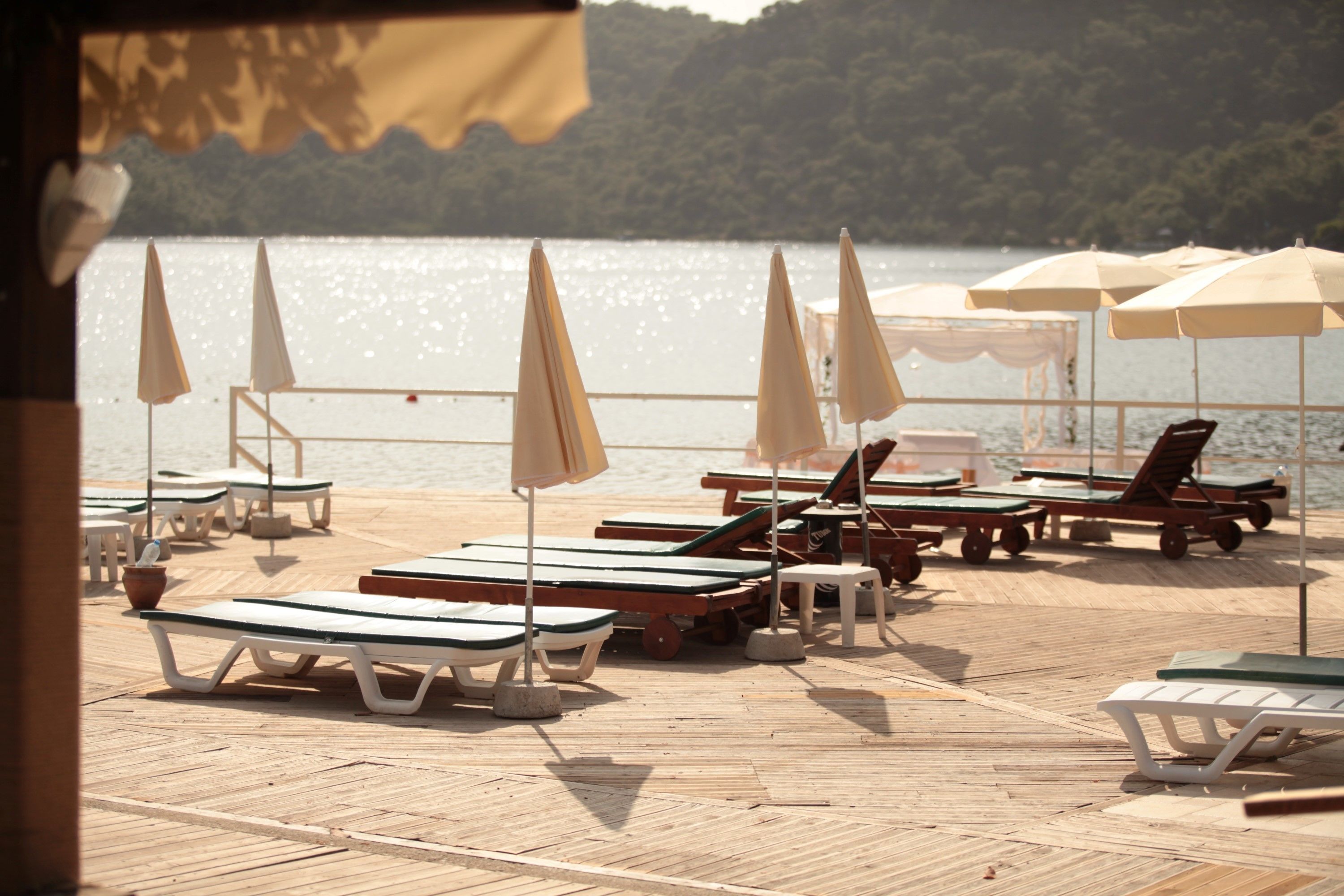 A wooden deck with lounge chairs and umbrellas, overlooking a body of water.