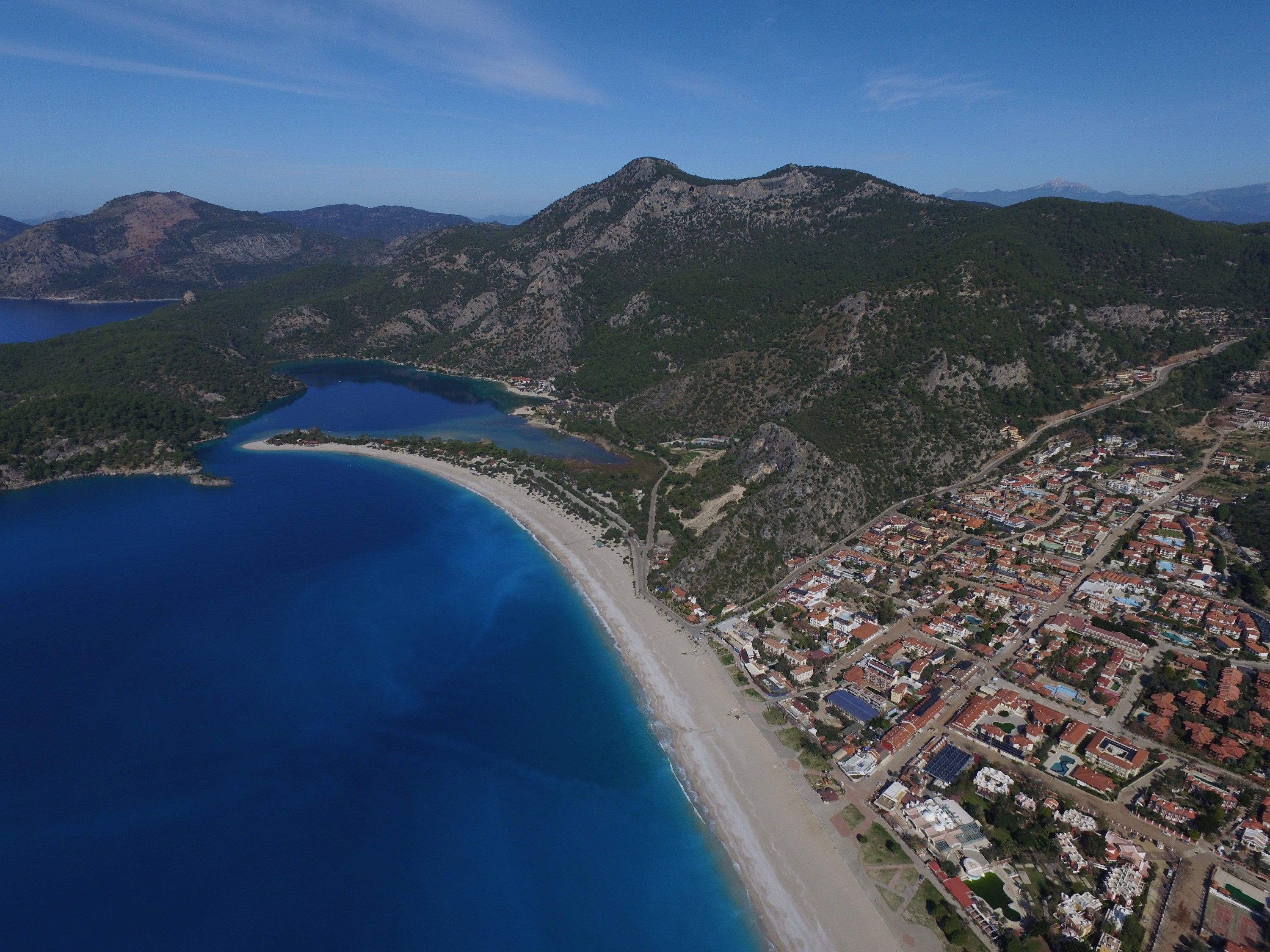 An aerial view of a coastal town with a beach, mountains, and a bay.