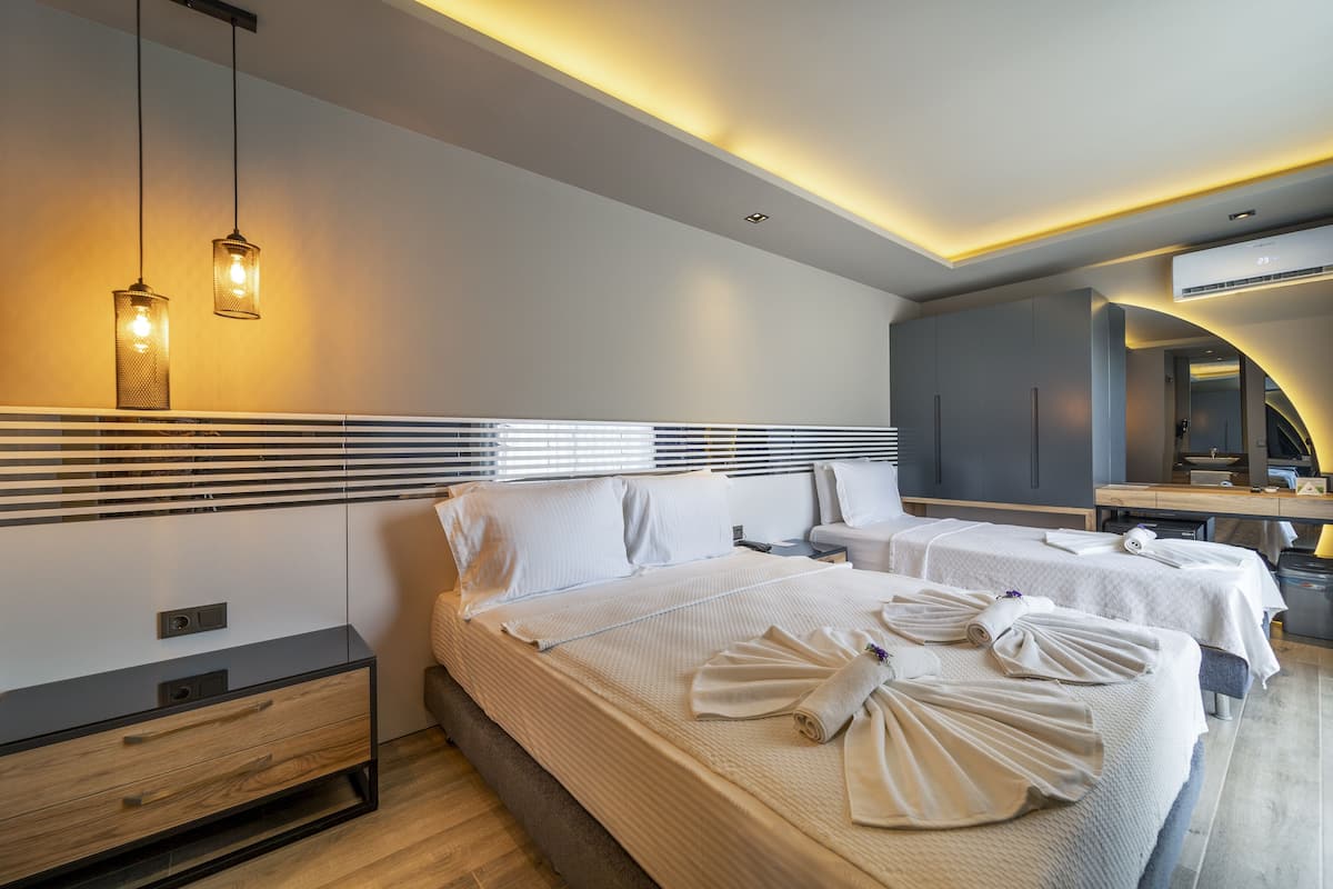 Una habitación de hotel moderna con dos camas, una mesita de noche, un armario y un baño con espejo y lavabo.