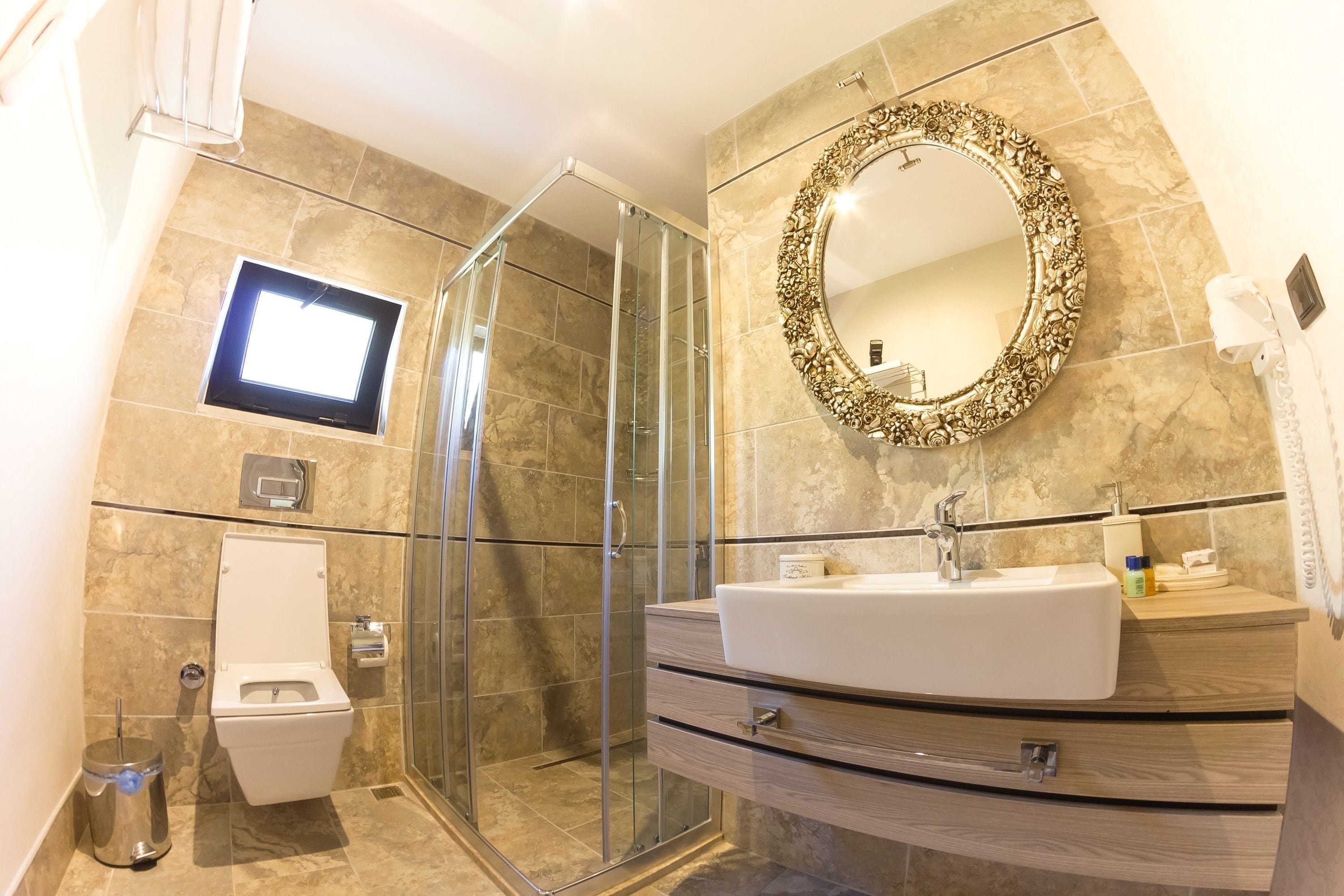 Un baño moderno con ducha envuelta en vidrio, inodoro, lavabo con tocador y un espejo grande y decorativo.