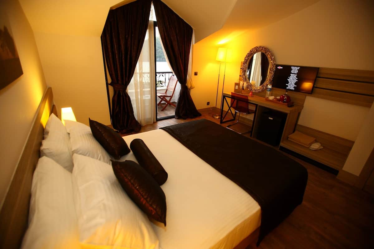 Habitación de hotel con una cama grande, un escritorio con espejo, una televisión y un balcón con una silla.