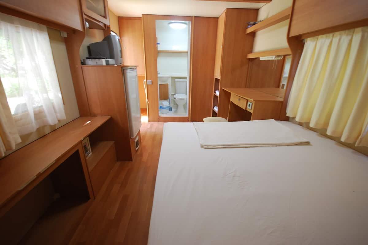 Un dormitorio de autocaravana compacto con cama, escritorio pequeño y armario de almacenamiento.