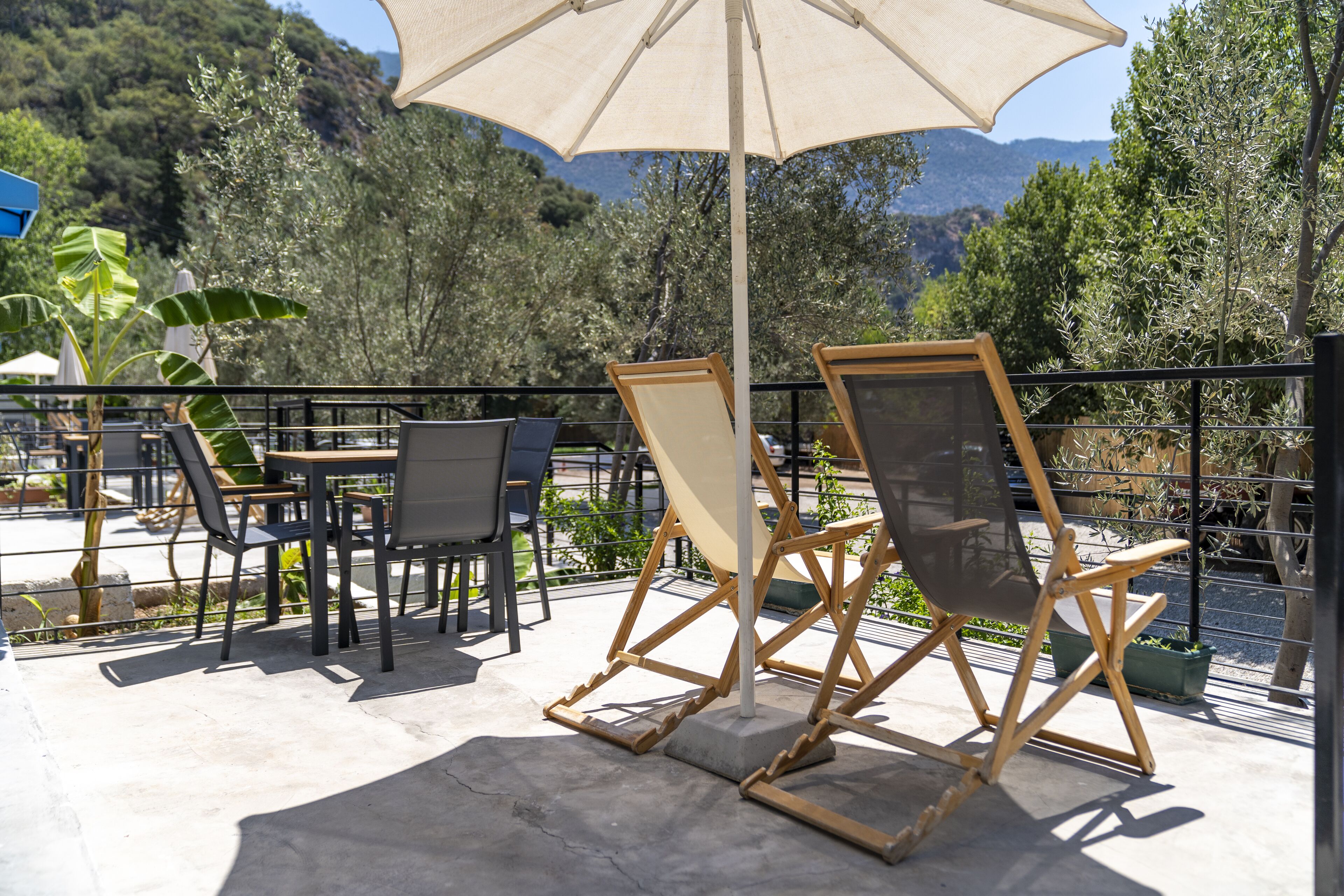 Un espace extérieur aménagé avec des tables et des chaises, un grand parasol et une vue sur les arbres et les collines.