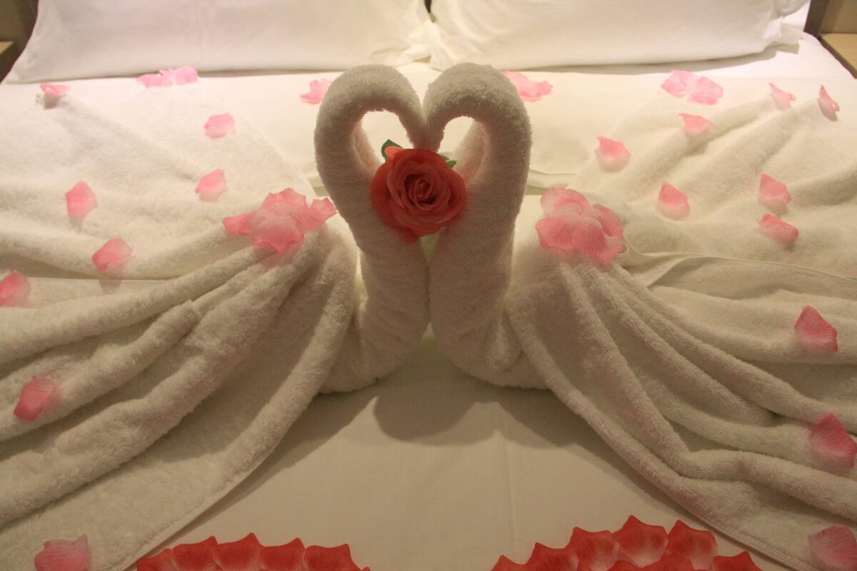 A bed with a white sheet and pink rose petals scattered across it.