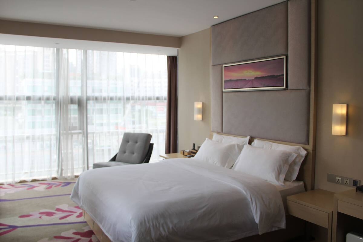 A hotel room with a large bed, a chair, a nightstand, and a painting on the wall.