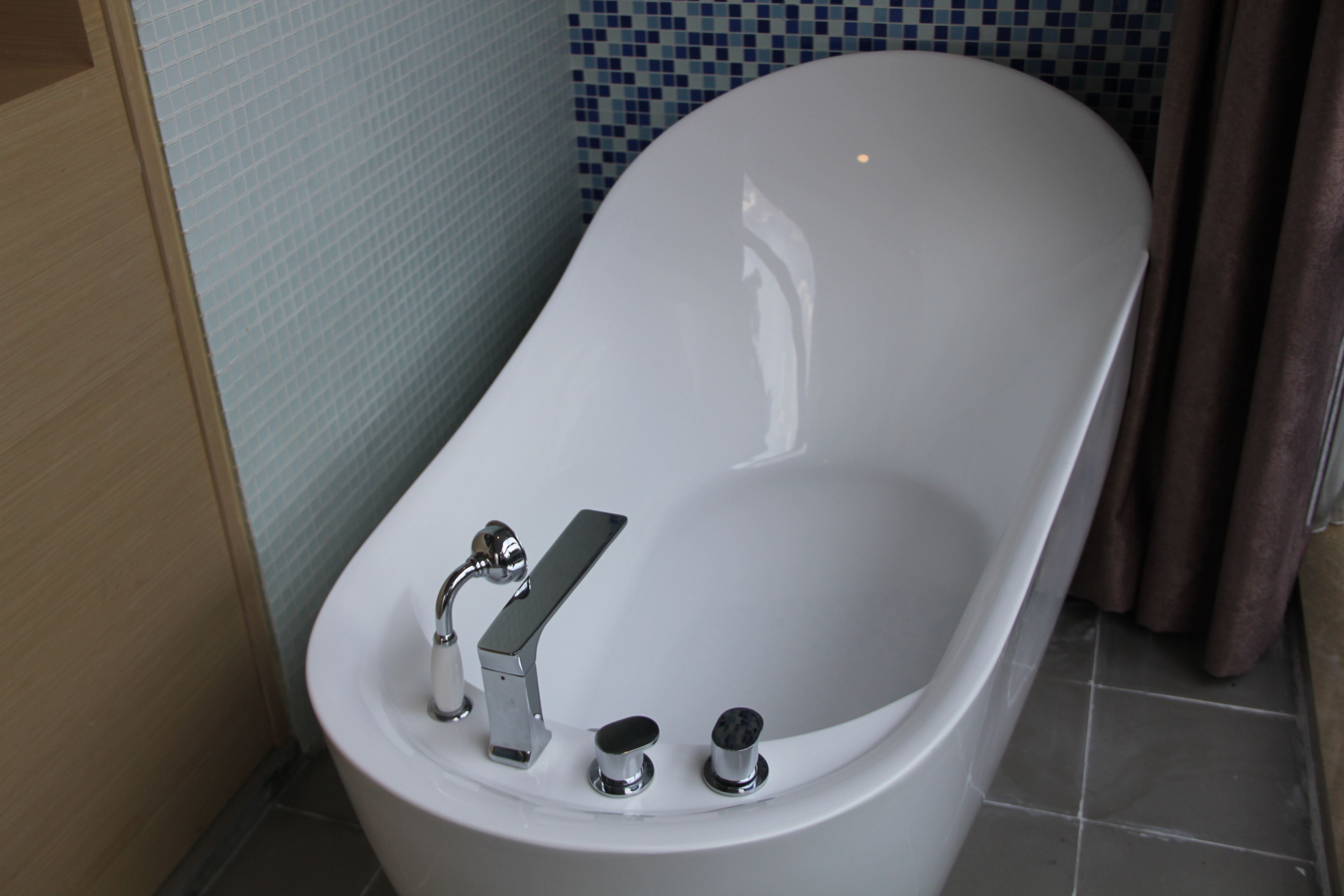 Un baño moderno con una bañera independiente, un cabezal de ducha de mano y un grifo de pared.