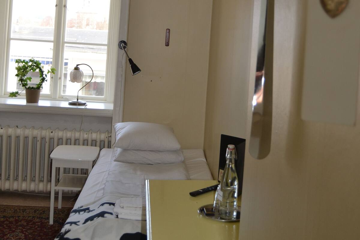 A bedroom with a bed, a bedside table, a lamp, a window with a view, and a radiator.