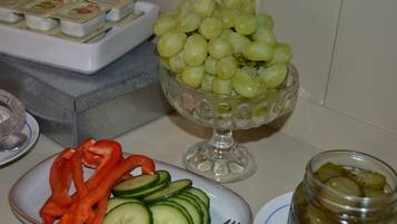 A table with a bowl of green grapes, a plate with sliced cucumbers and red bell peppers, and a jar of pickles.