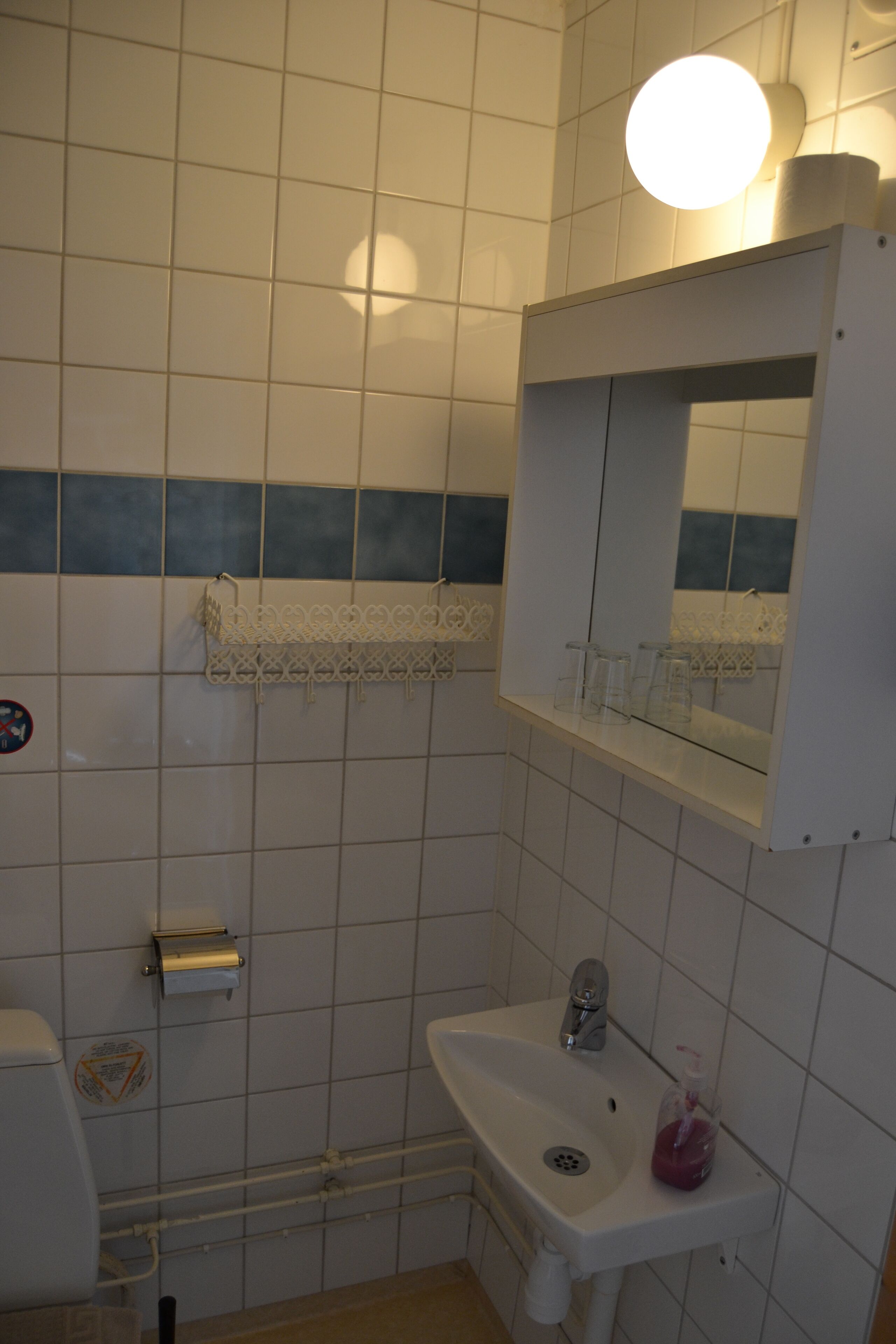 Um banheiro com azulejos brancos, pia, espelho e porta-toalhas.