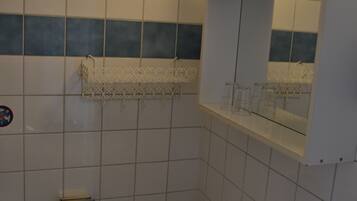 Um banheiro com azulejos brancos, pia, espelho e porta-toalhas.