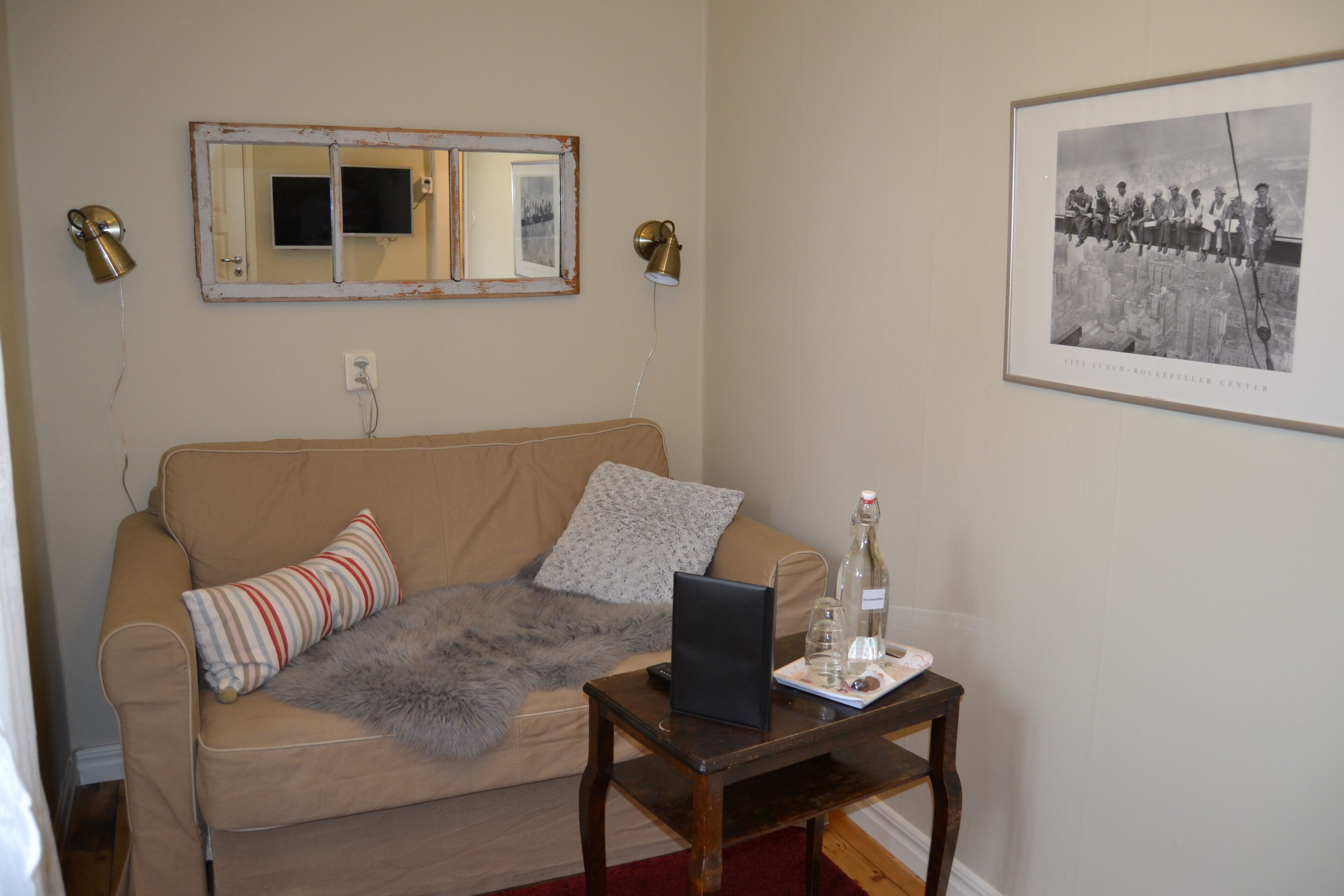 Un salon avec un canapé beige, un miroir, une photographie encadrée et une petite table sur laquelle se trouvent un ordinateur portable et des lunettes.