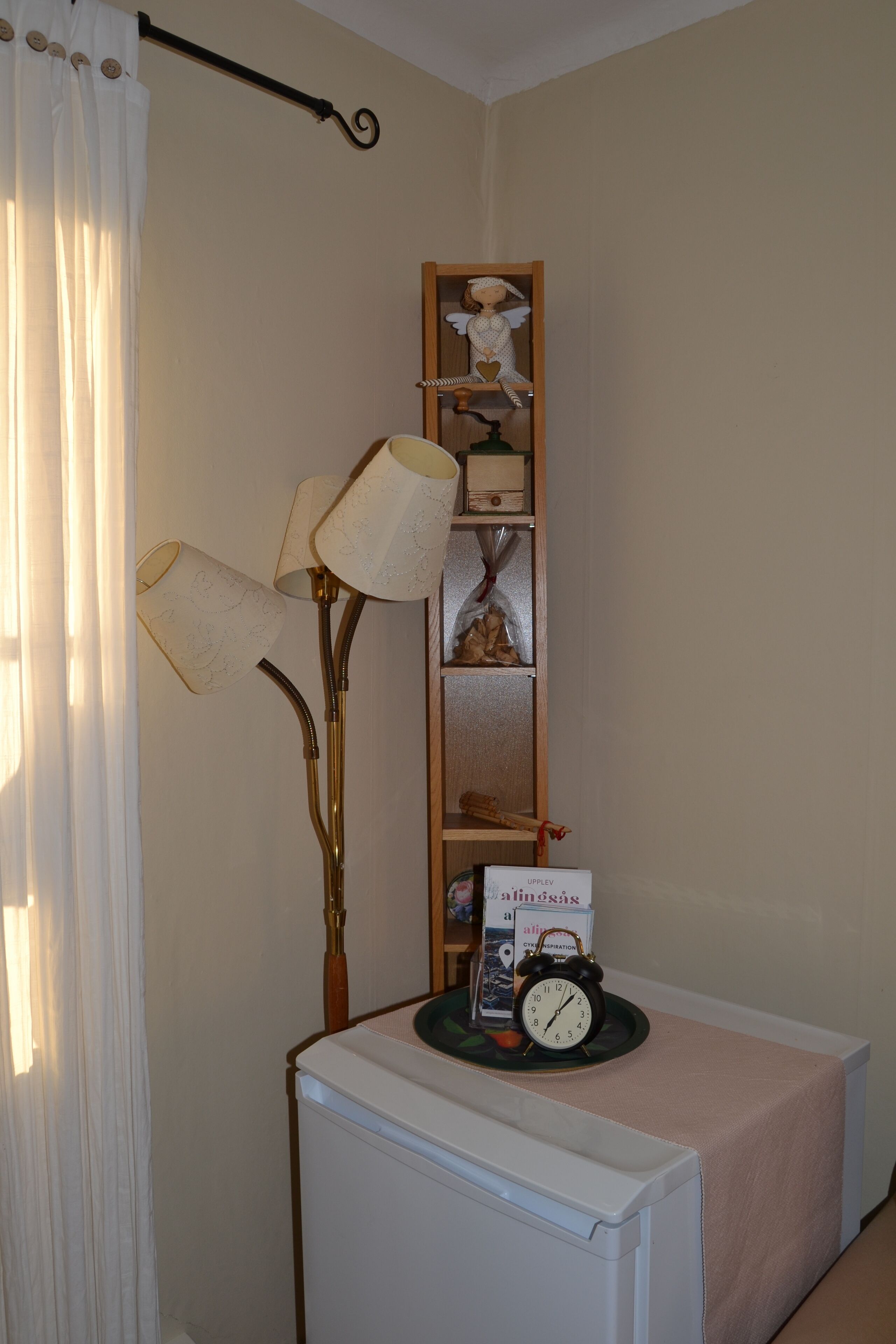 Une pièce avec un radiateur, une lampe, une étagère ornée d’objets décoratifs et une horloge posée sur une table.