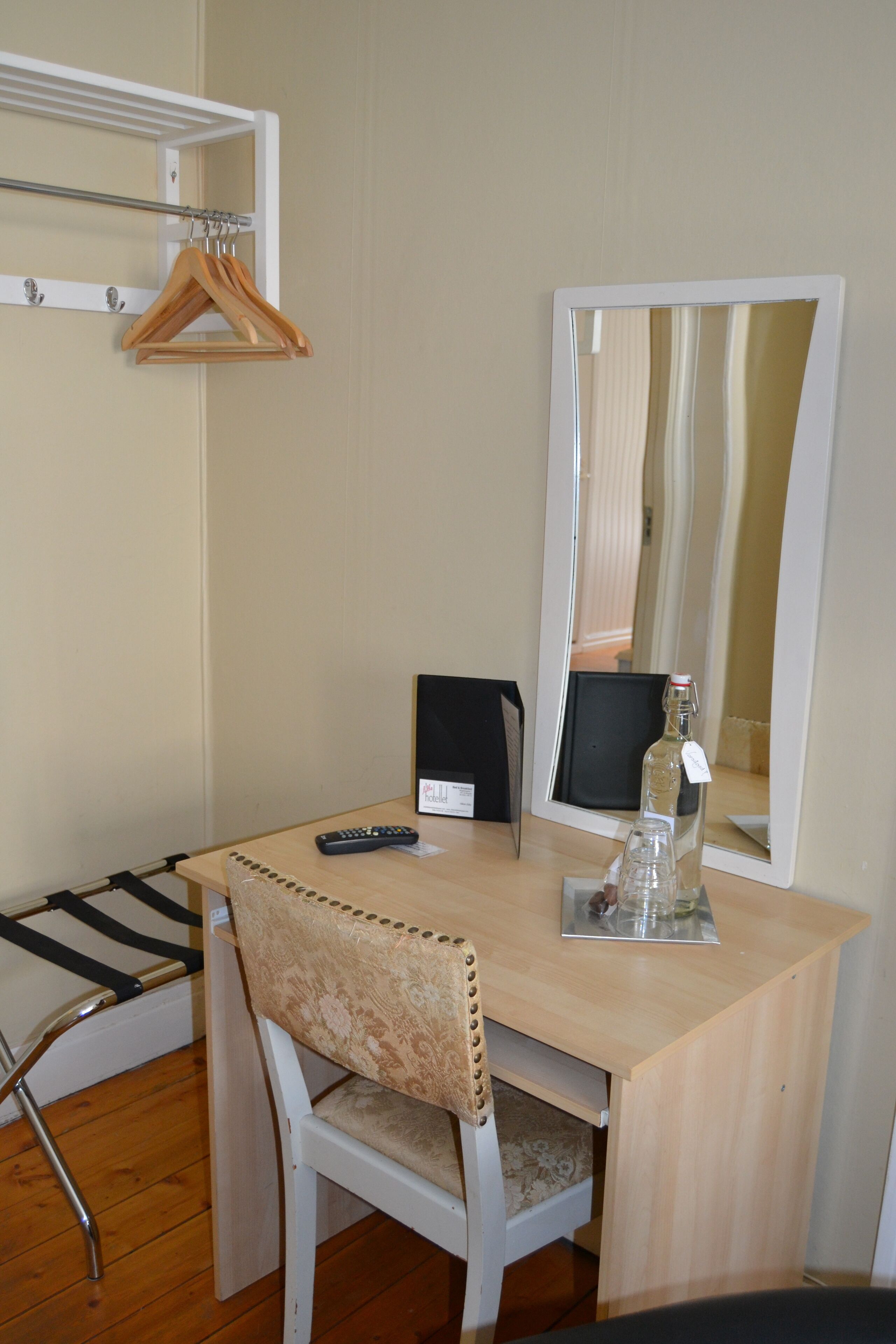 Una habitación pequeña con un escritorio de madera, una silla, un espejo, una botella y un control remoto.