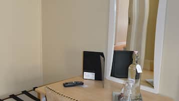 Una habitación pequeña con un escritorio de madera, una silla, un espejo, una botella y un control remoto.
