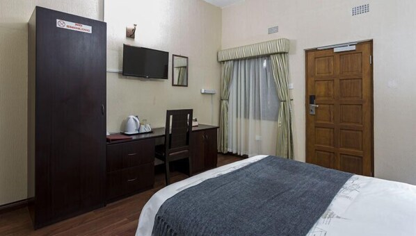 Habitación de hotel con cama, escritorio, silla, armario, televisor y puerta.