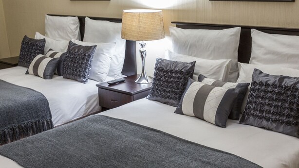 Een hotelkamer met twee bedden, een nachtkastje, een lamp en meerdere kussens.