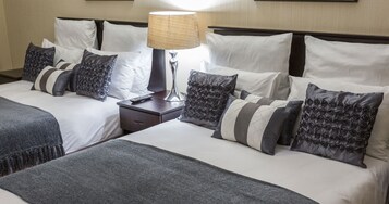 Una habitación de hotel con dos camas, una mesita de noche, una lámpara y varias almohadas.