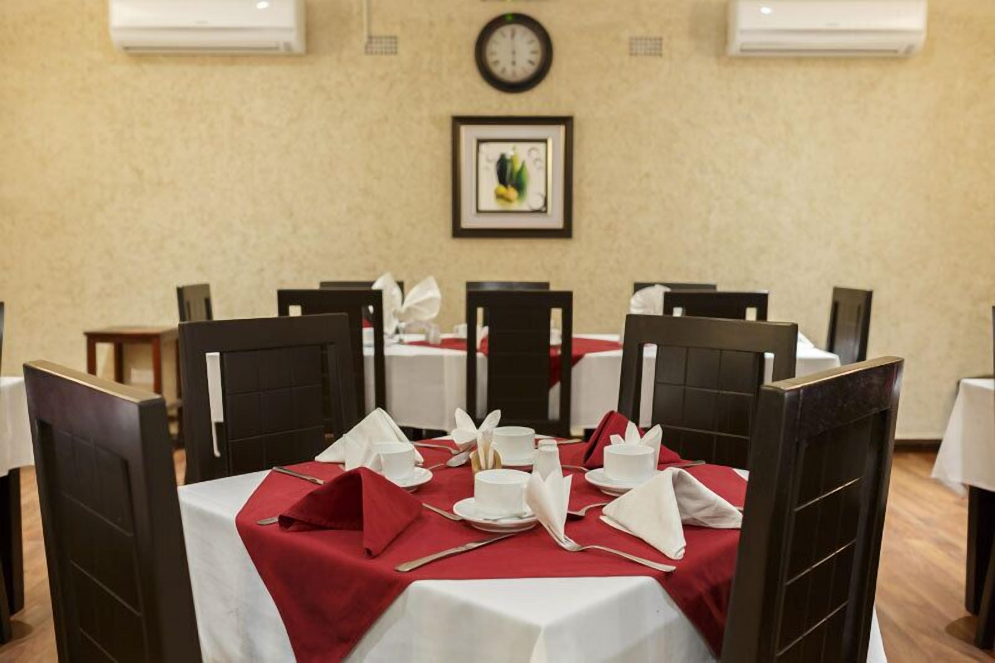 Comedor con mesas dispuestas para cuatro, cada una con mantel blanco y servilletas rojas.