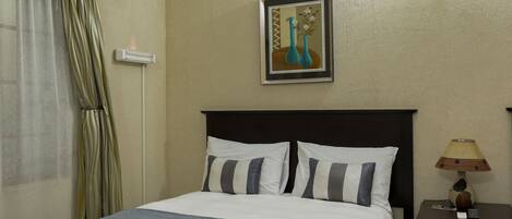 A hotel room with a bed, a nightstand, a lamp, and a painting on the wall.