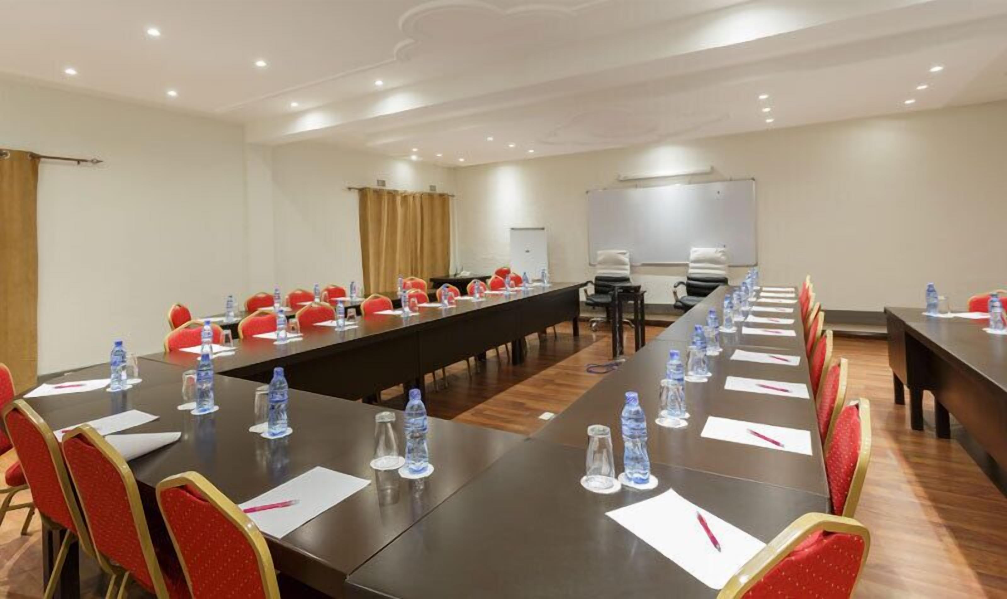 A conference room with long tables, red chairs, water bottles, and a whiteboard.