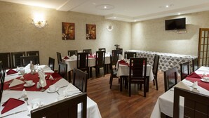 Een eetruimte met meerdere tafels gedekt voor service, een televisie aan de muur en een tafel met een geruit tafelkleed.