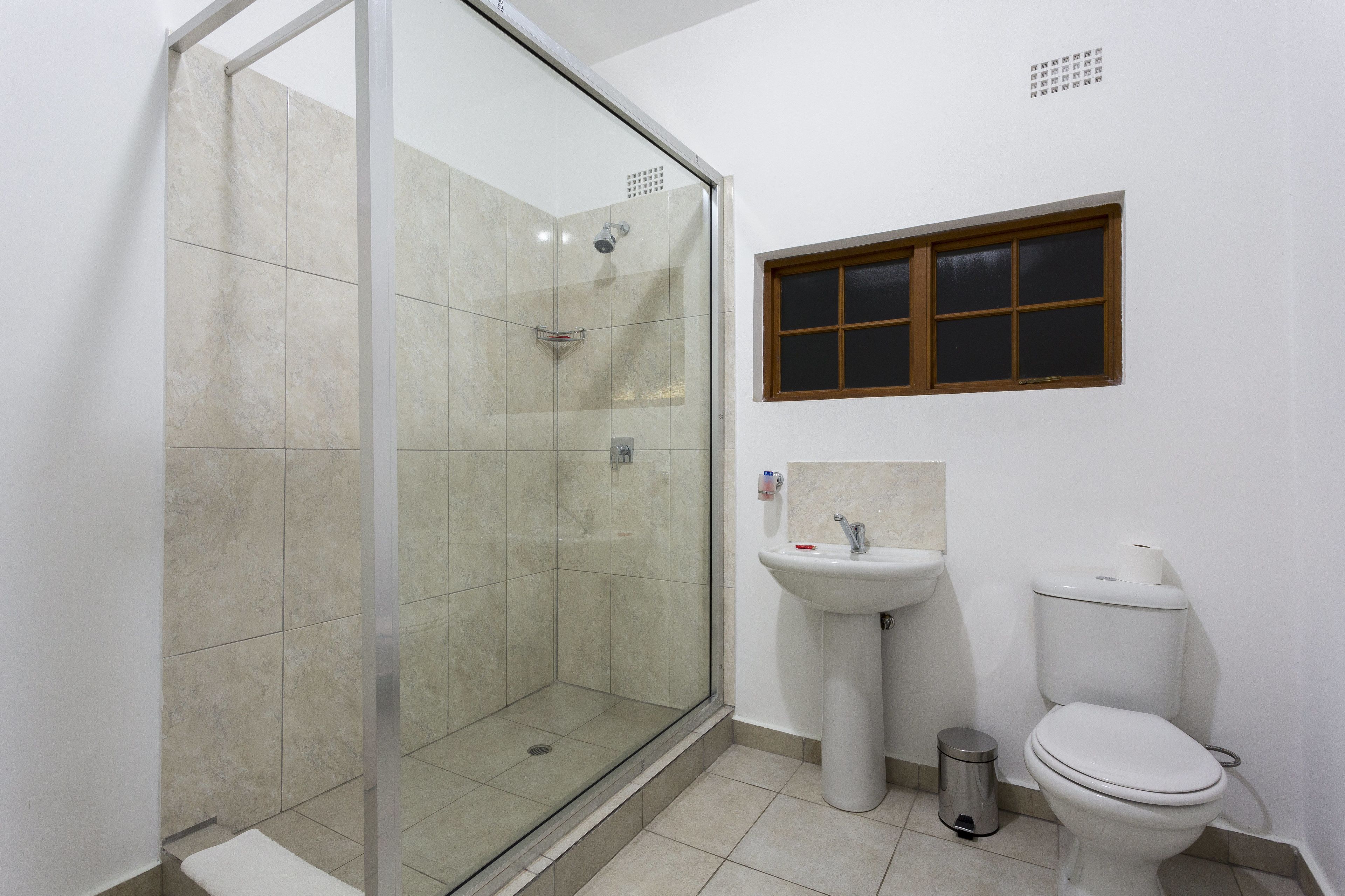 A bathroom with a glass-enclosed shower, a pedestal sink, and a toilet.