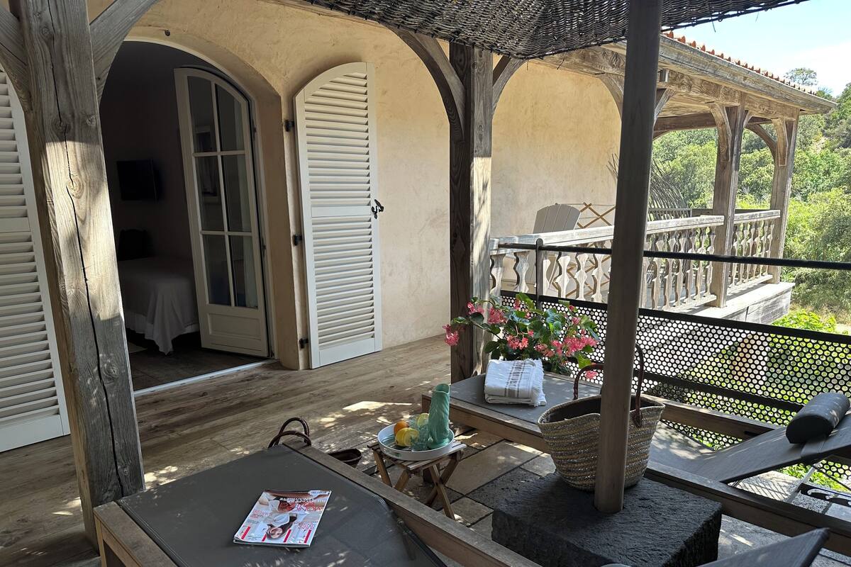 A wooden deck with outdoor seating, a covered area, and a view of a lush garden.