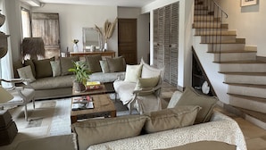 A spacious living room with a large sofa, a coffee table, and a staircase leading to an upper floor. - Le clos des sept palmiers (Cavalaire-sur-Mer)