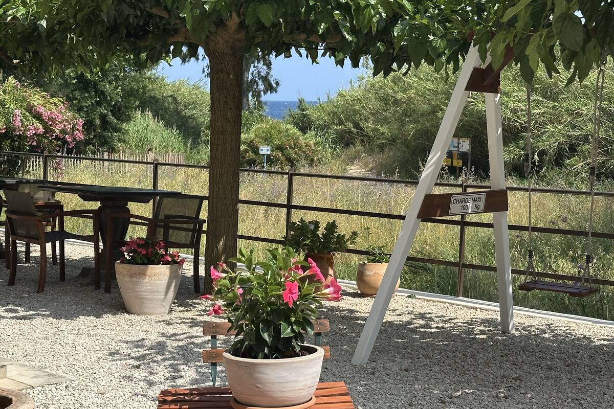 A patio area with a wooden bench, a table, and chairs. There are potted plants and a swing. A sign indicates a charge for a service.