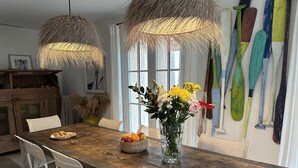 A dining area with a wooden table, chairs, a vase of flowers, and a wall with colorful paddles. - Le clos des sept palmiers (Cavalaire-sur-Mer)