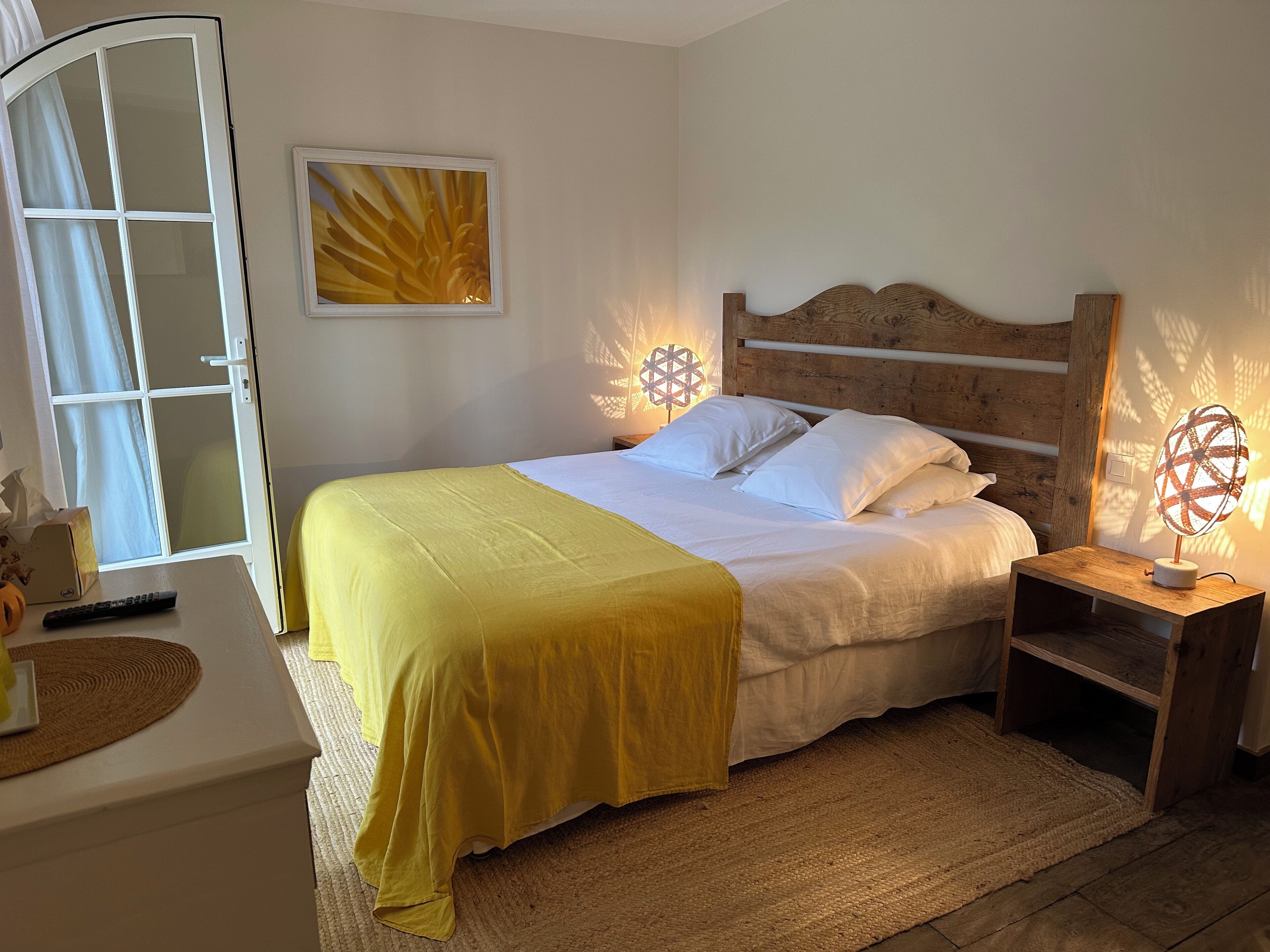 A bedroom with a bed, bedside tables, a nightstand, a wall-mounted lamp, and a window with curtains.