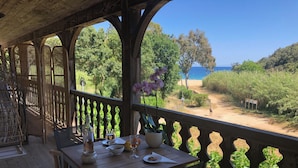 A wooden deck with a table set for dining, overlooking a beach and forested area. - Le clos des sept palmiers (Cavalaire-sur-Mer)