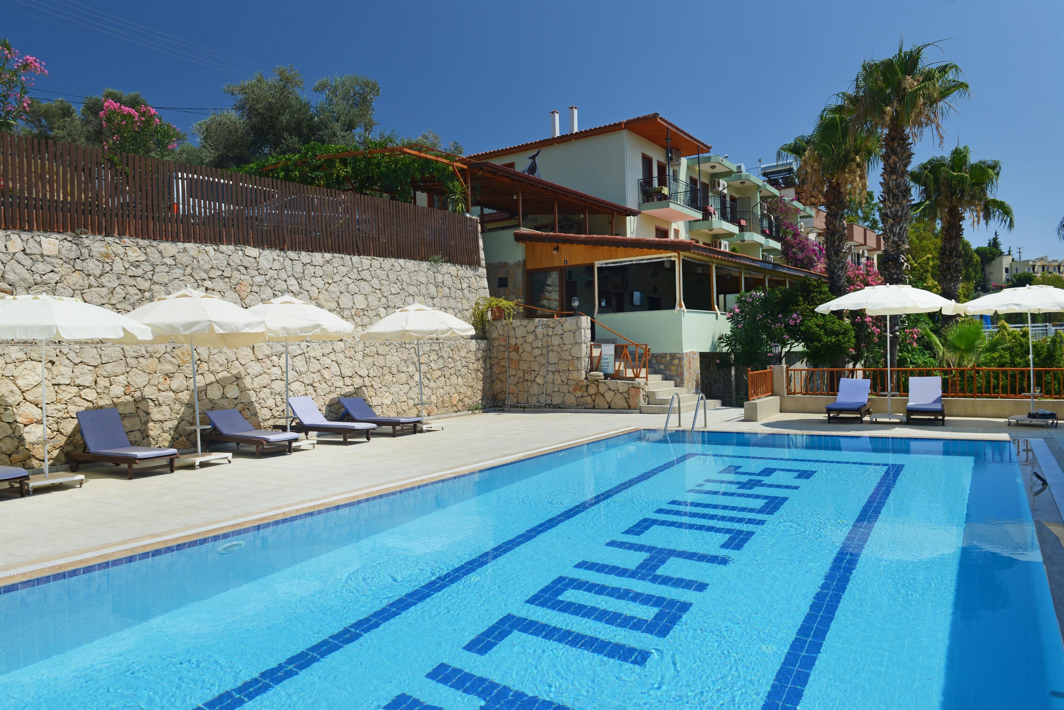 Ein Pool mit Liegestühlen und Sonnenschirmen, umgeben von Steinmauern und einem Holzzaun.