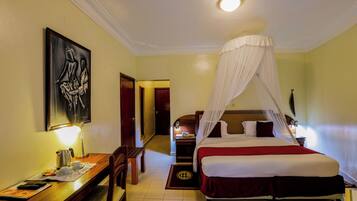 A hotel room with a bed, a desk with a lamp, a chair, and a painting on the wall.