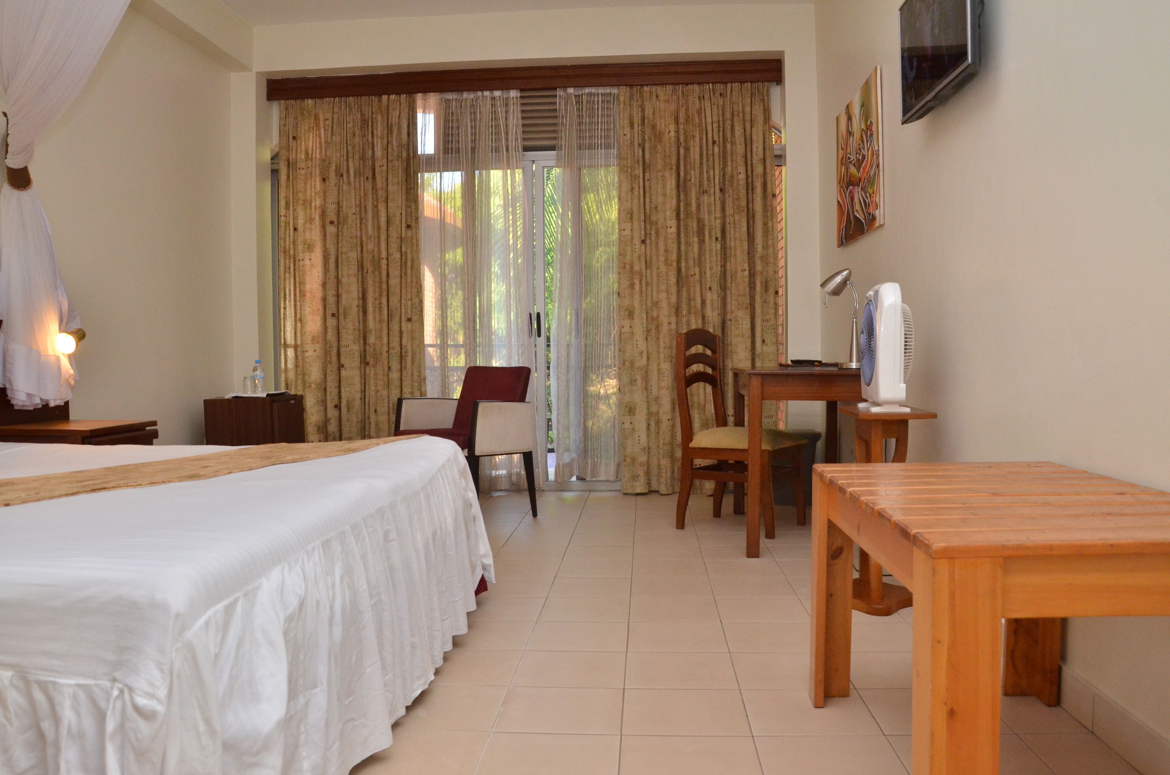 A hotel room with a bed, a desk, a chair, a table, a TV, and curtains.